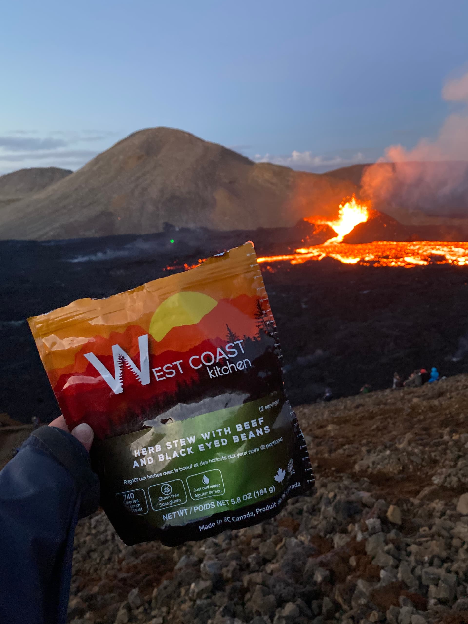 Hand holding WCK Herb Stew pouch in front of volcano at dusk