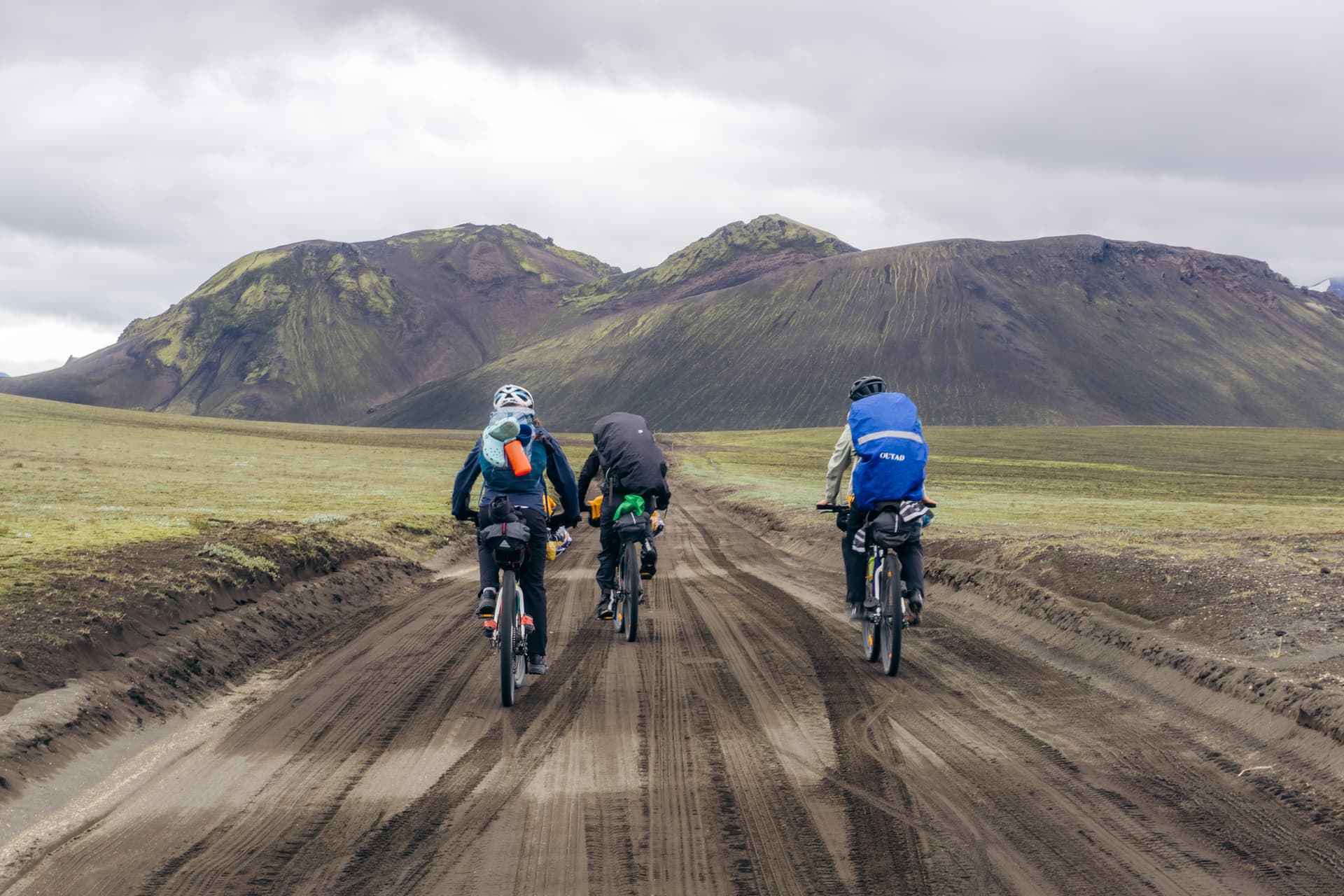 Three cyclists on a gravel road through green Icelandic mountains
